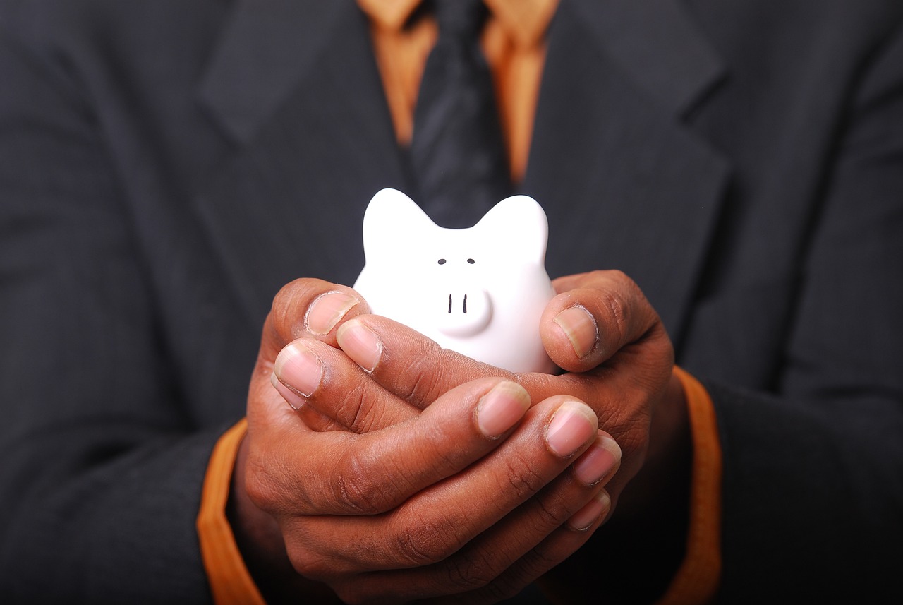 A small white piggy bank sitting on a wooden surface, representing careful, low-fee long-term saving.