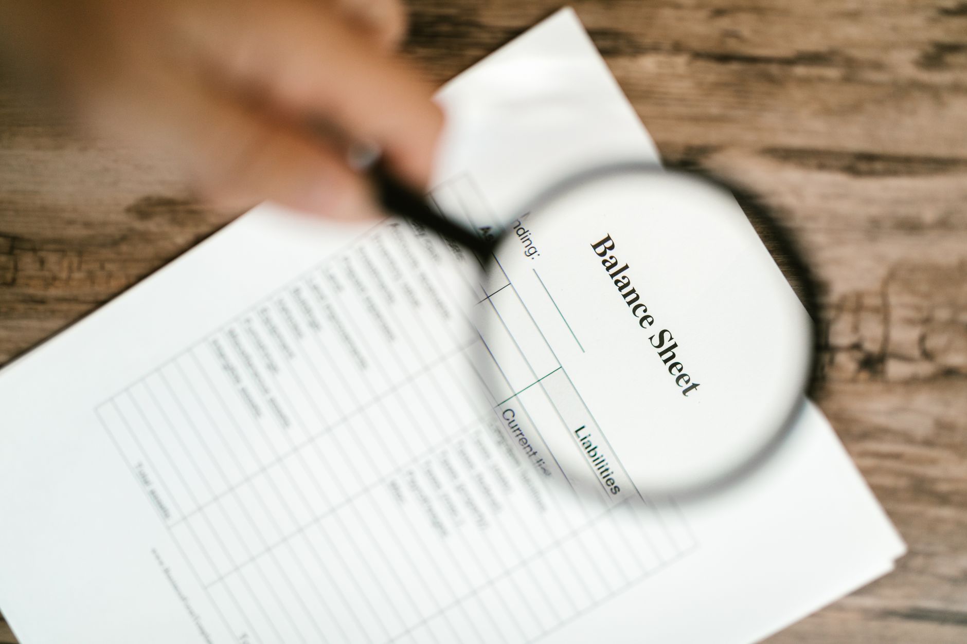 A close-up view of a person using a magnifying glass to inspect the account history section of a paper credit report