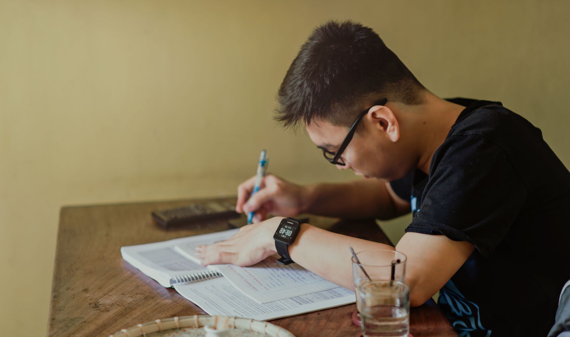 A young student sitting at a wooden desk reviewing financial documents and student loan paperwork