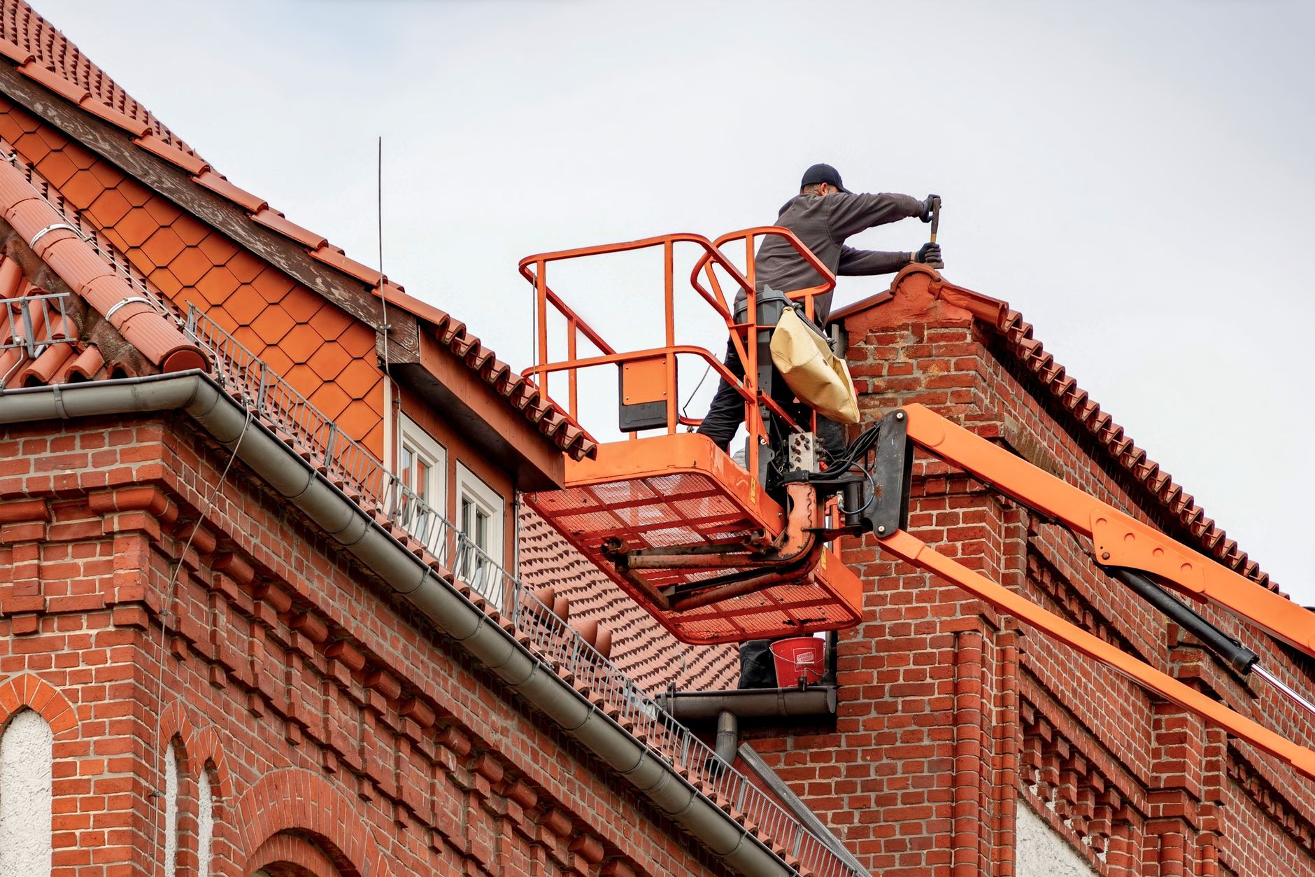 A homeowner cleaning leaves out of roof gutters during the autumn season