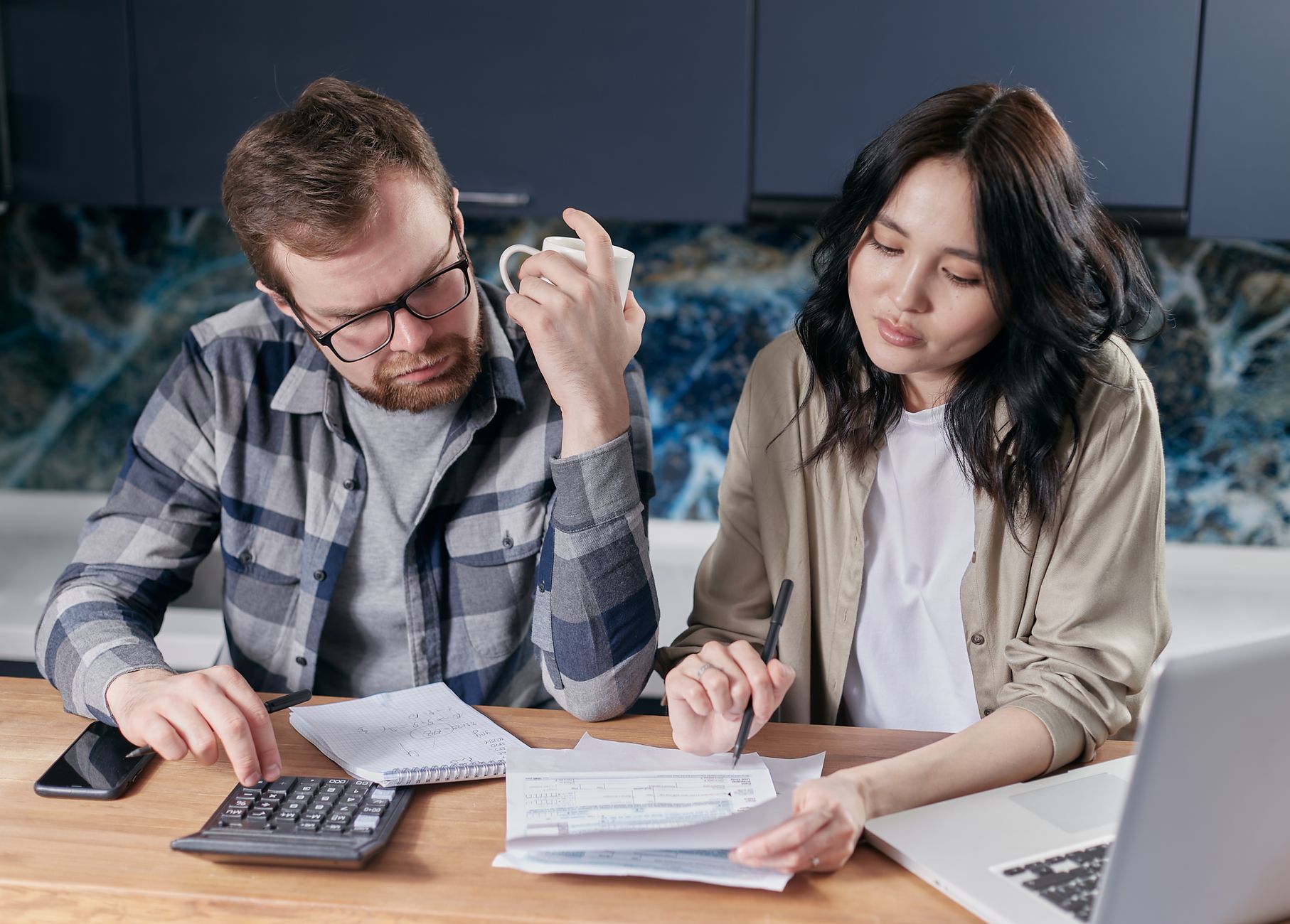 A young couple sitting at a kitchen island reviewing financial documents on a tablet